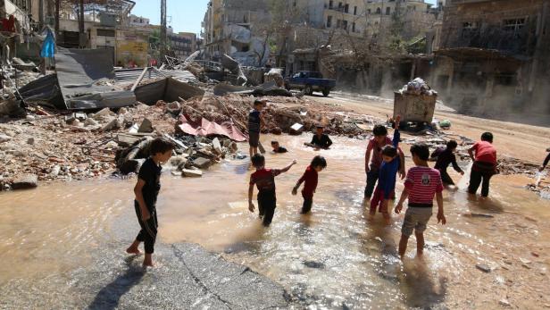 Aleppo:; Kinder spielen in einem gefluteten Bombenkrater.