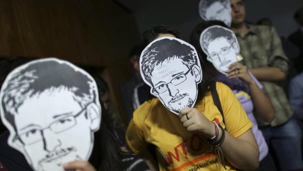 Menschen halten Pappmasken mit dem Gesicht von Edward Snowden hoch.