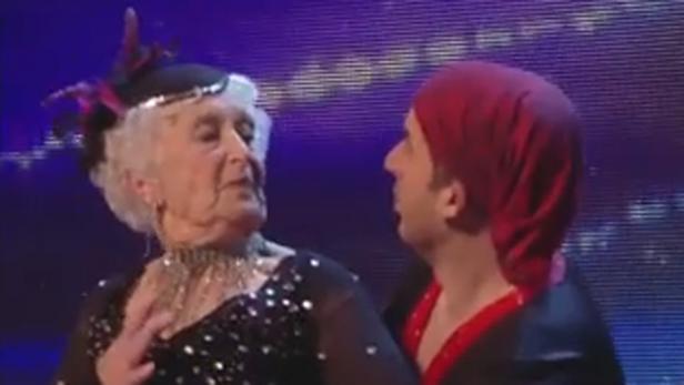 Eine ältere Frau mit Hut tanzt mit einem Mann mit rotem Turban.