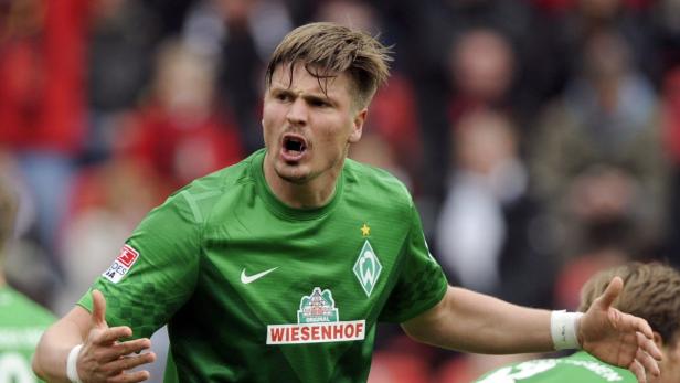 Ein Fußballspieler in grünem Trikot gestikuliert auf dem Spielfeld.