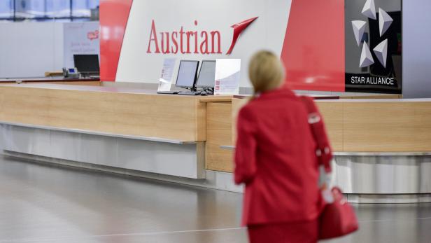 Eine Frau in roter Jacke vor einem Austrian Airlines Check-in-Schalter.