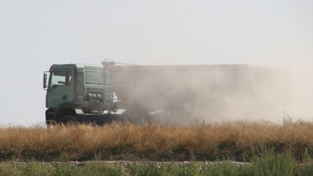 Ein grüner Muldenkipper erzeugt eine Staubwolke auf einem Feld.