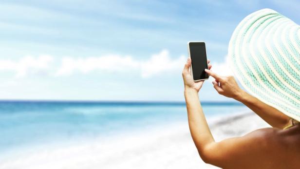 Eine Frau mit Hut macht ein Foto mit ihrem Smartphone am Strand.