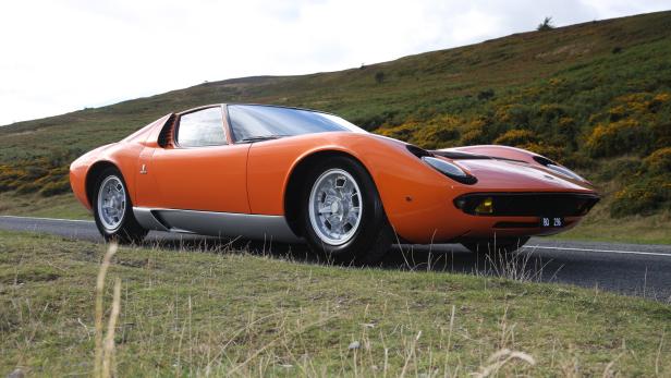 Ein orangefarbener Lamborghini Miura vor einer hügeligen Landschaft.