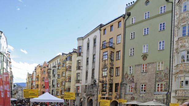 Bunte Häuserzeile in Innsbruck mit Menschen und Werbebannern im Vordergrund.