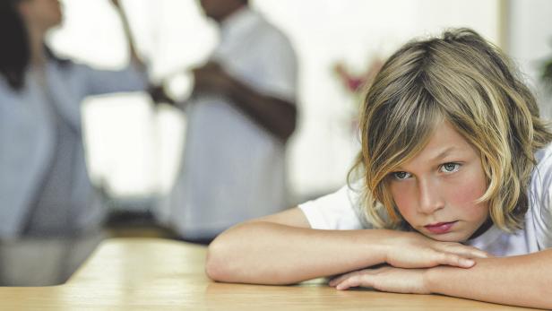 Worried looking boy with his fighting parents behind him