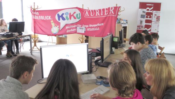 Eine Gruppe von Kindern arbeitet an Computern unter einem „KiKu Kurier“-Banner.