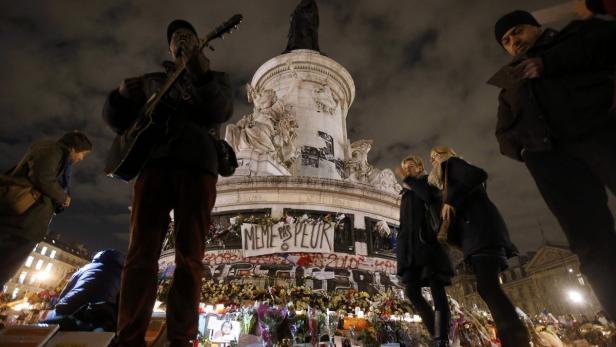 Menschen gedenken an einem Denkmal in Paris mit Blumen, Fotos und Kerzen.