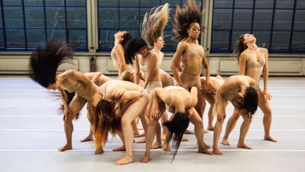 Eine Gruppe Tänzerinnen in beigefarbener Kleidung führt eine synchrone Choreografie auf.