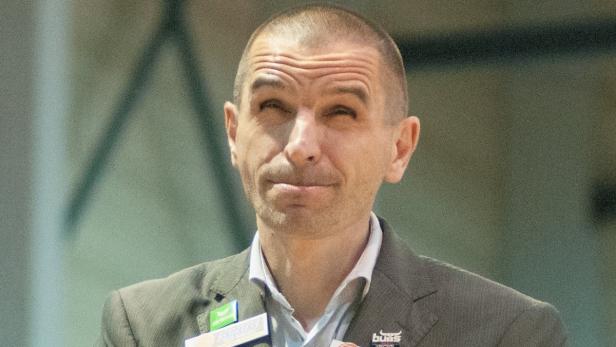 Ein Mann in einem Anzug mit einem Namensschild lächelt leicht.