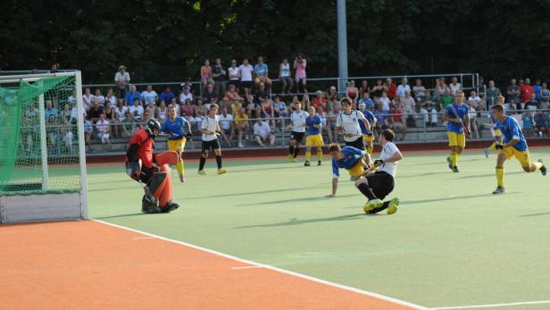 Ein Hockeyspiel mit Spielern in blauen und weißen Trikots vor einer Zuschauermenge.