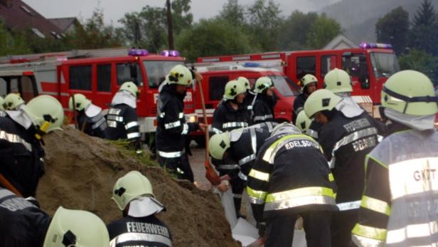 Eine Gruppe Feuerwehrleute arbeitet mit Schaufeln an einem Erdhaufen vor roten Feuerwehrfahrzeugen.