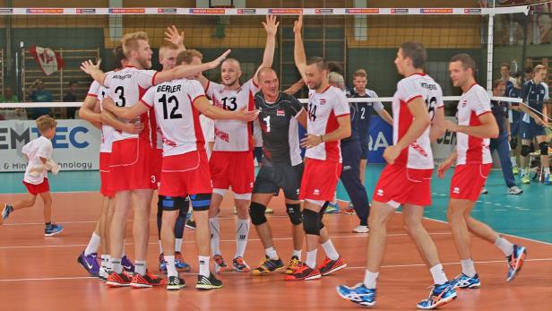 Ein Volleyballteam umarmt sich auf dem Spielfeld, während ein Trainer daneben steht.