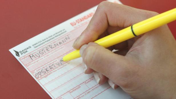 Eine Hand füllt mit einem gelben Stift einen Überweisungsträger der BAWAG P.S.K. aus.