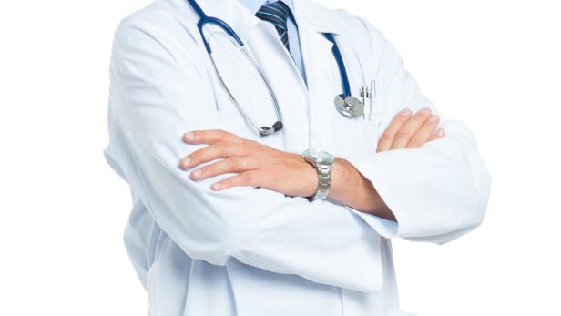 Ein Arzt mit verschränkten Armen, Stethoskop und Uhr vor weißem Hintergrund.