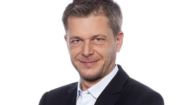Ein Mann mit Anzug und Hemd lächelt in die Kamera.