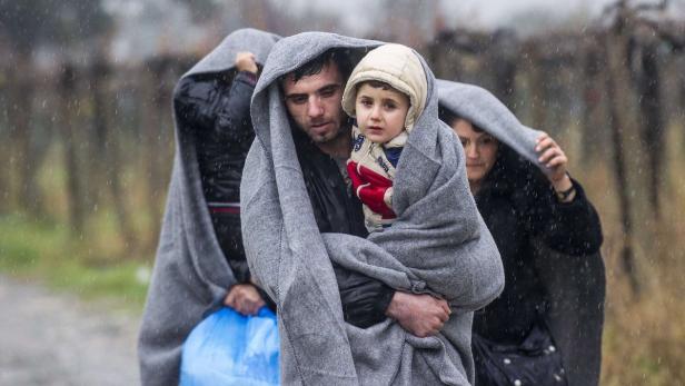 Eine Familie geht im Regen, in graue Decken gehüllt.