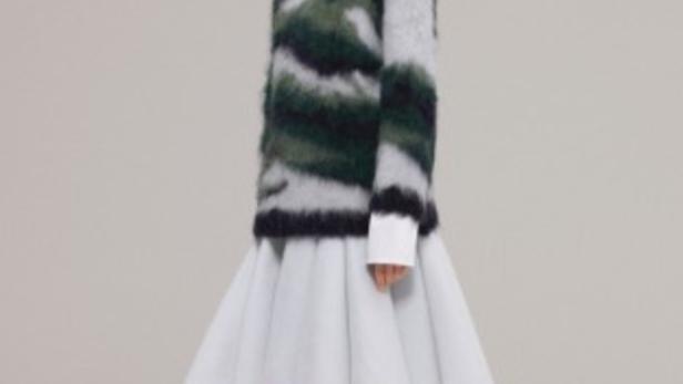 Eine Frau trägt einen gestreiften Pullover, einen weißen Rock und schwarze Stiefel.