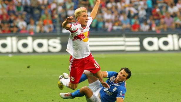Ein Fußballspieler springt über einen am Boden liegenden Gegenspieler.