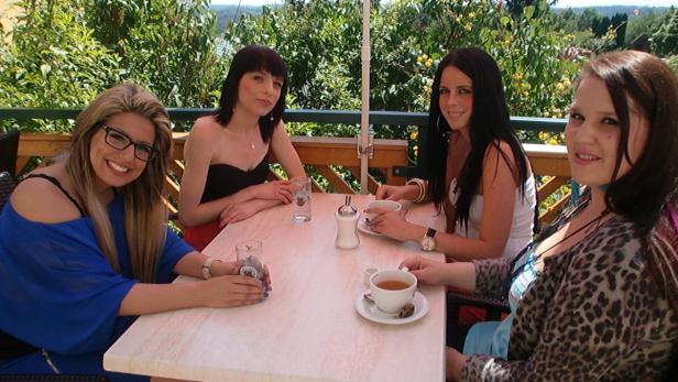 Vier junge Frauen sitzen auf einer Terrasse und trinken Tee.