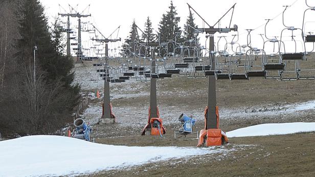 Ein Skilift steht auf einer Wiese mit Schneekanonen.