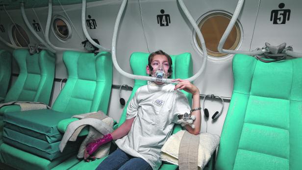 Ein Jugendlicher sitzt mit einer Sauerstoffmaske in einer hyperbaren Kammer.
