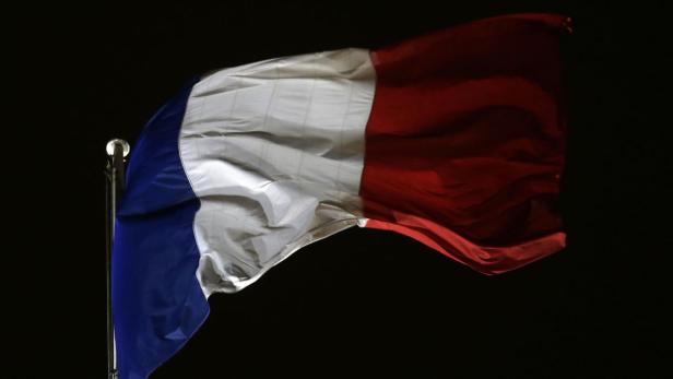 Die französische Flagge weht im Wind vor einem dunklen Hintergrund.