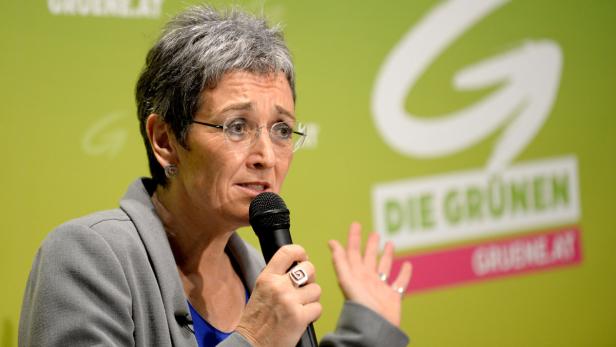 Eine Frau mit Brille spricht vor einem Hintergrund der Grünen in ein Mikrofon.