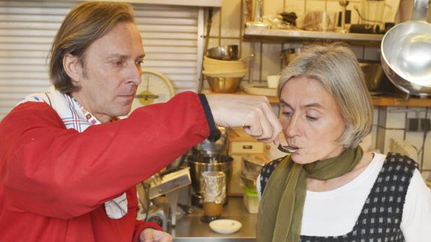 Ein Mann füttert eine Frau mit einem Löffel in einer Küche.