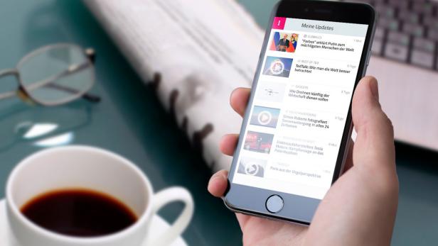 Ein Smartphone zeigt einen Nachrichten-Feed neben einer Tasse Kaffee und einer Zeitung.
