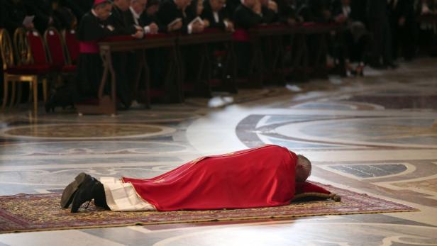 Papst Franziskus liegt während einer Zeremonie auf einem Teppich.