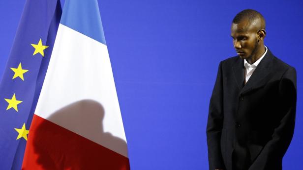 Ein Mann in Anzug steht vor der Europa- und Frankreichflagge.