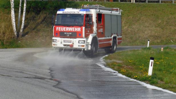 Ein rotes Feuerwehrfahrzeug der Marke MAN reinigt eine Straße mit Wasser.