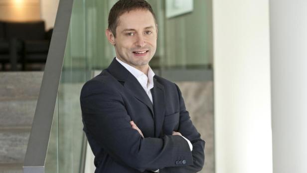 Ein Mann im Anzug steht mit verschränkten Armen vor einer Treppe.