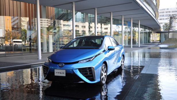 Ein blauer Toyota Mirai steht vor einem modernen Gebäude im Wasser.