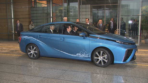 Ein blauer Toyota Mirai wird von mehreren Personen umringt.