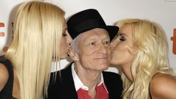 Hugh Hefner wird von zwei blonden Frauen auf die Wange geküsst.
