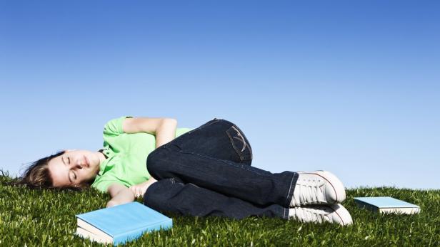 Pretty brunette lying on grass asleep with books