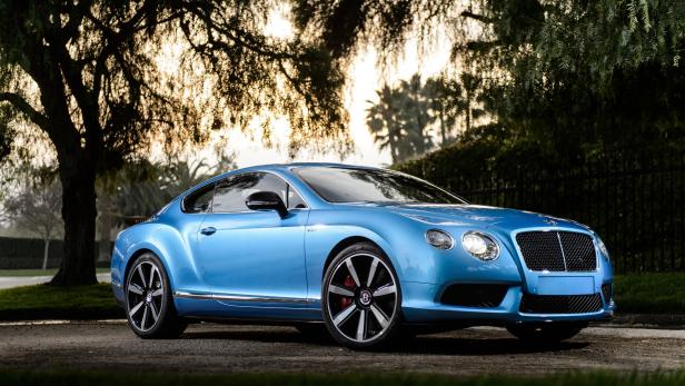 Ein hellblauer Bentley Continental steht vor Bäumen im Gegenlicht.