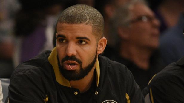 Drake sitzt mit einem Zahnstocher im Mund auf einem Stuhl.
