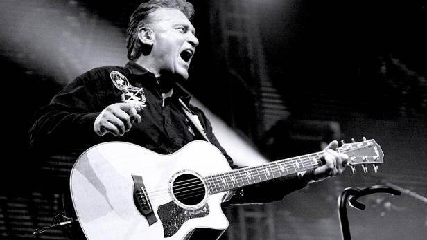 Ein Mann mit Gitarre singt auf einer Bühne.