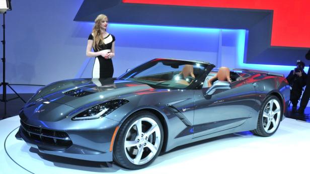 Eine graue Corvette wird auf einer Automesse von einer Frau präsentiert.