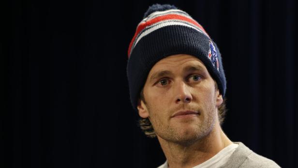 Tom Brady mit einer blau-rot-weißen Mütze vor einem dunklen Hintergrund.