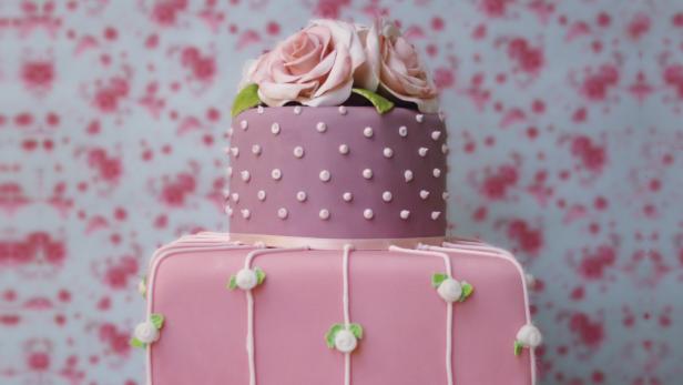 Ein zweistöckiger, rosa dekorierter Kuchen mit Rosen auf der Spitze.