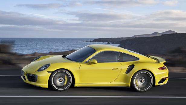 Ein gelber Porsche 911 fährt auf einer Küstenstraße.