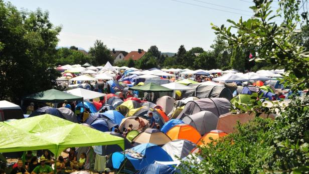 Ein Campingplatz mit vielen bunten Zelten unter blauem Himmel.