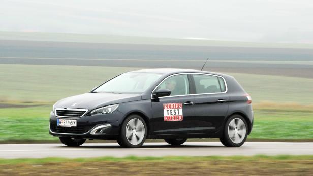 Ein schwarzer Peugeot 308 mit „Kurier Test Kurier“-Aufklebern fährt auf einer Landstraße.