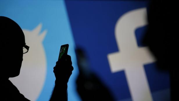 Men are silhouetted against a video screen with Facebook and Twitter logos as they pose with a Nokia Lumia 820 and Samsung Galaxy S4 in this photo illustration taken in the central Bosnian town of Zenica, August 14, 2013. REUTERS/Dado Ruvic (BOSNIA AND HERZEGOVINA - Tags: BUSINESS TELECOMS)