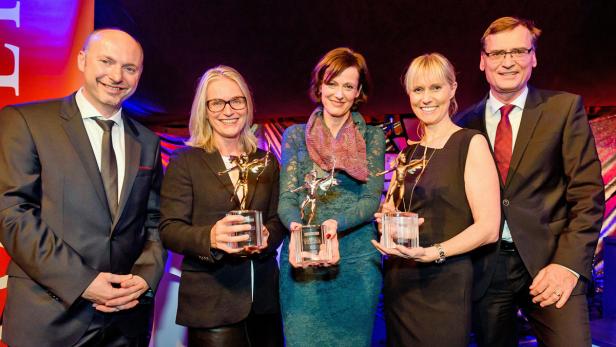 Fünf Personen posieren mit goldenen Statuen für ein Foto.