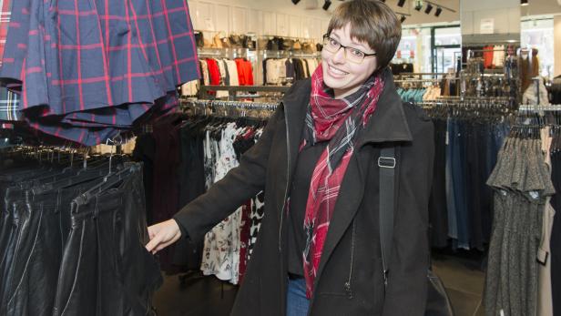 Eine Frau mit Brille und Schal steht in einem Bekleidungsgeschäft.